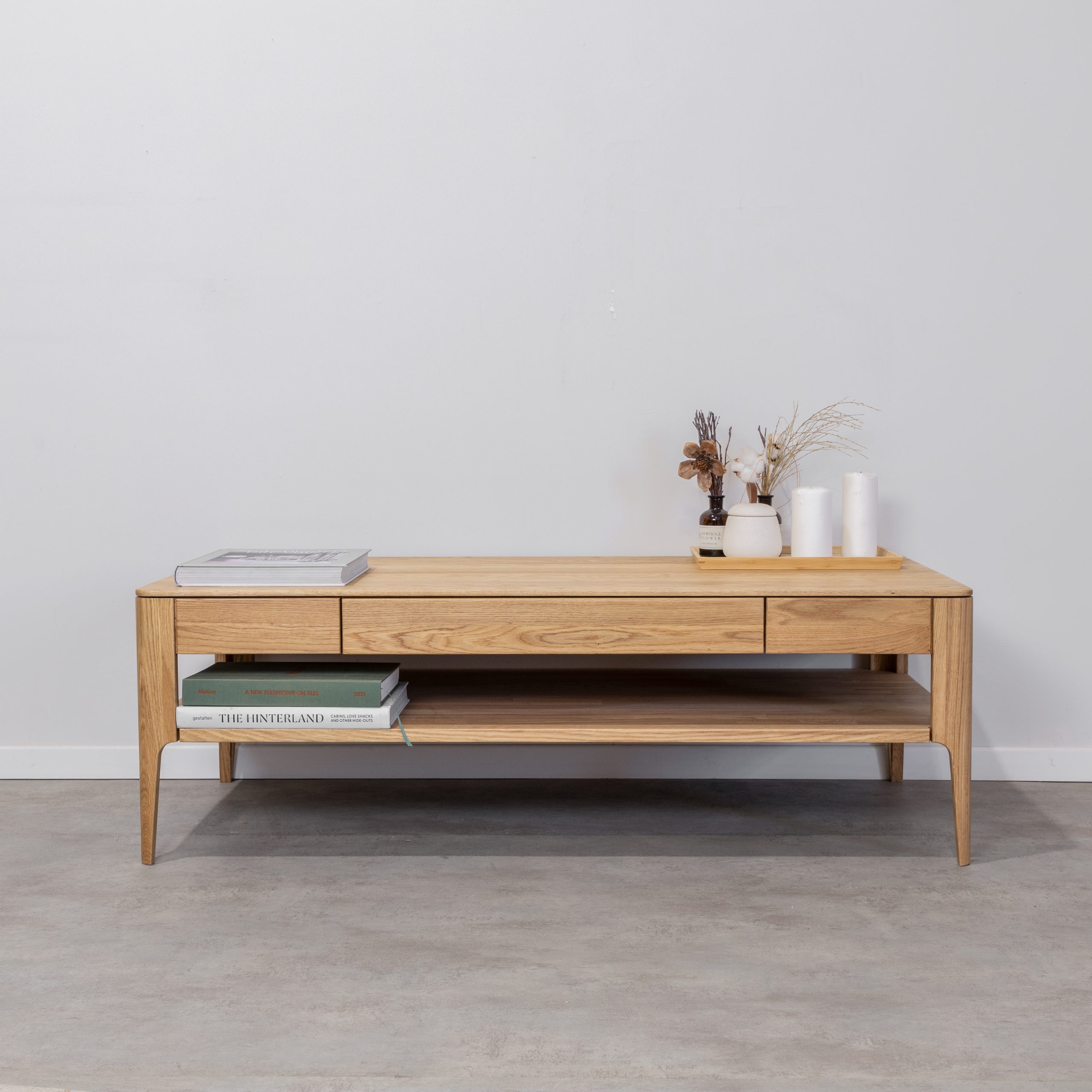 שולחן סלון מוריץ מעץ אלון מלא עם ספרים, אגרטלים ופרחים מיובשים על רקע קיר לבן ורצפה אפורה.